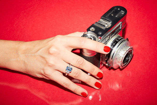 Hand wearing a white gold ring with three baguette blue gemstones beside a vintage camera