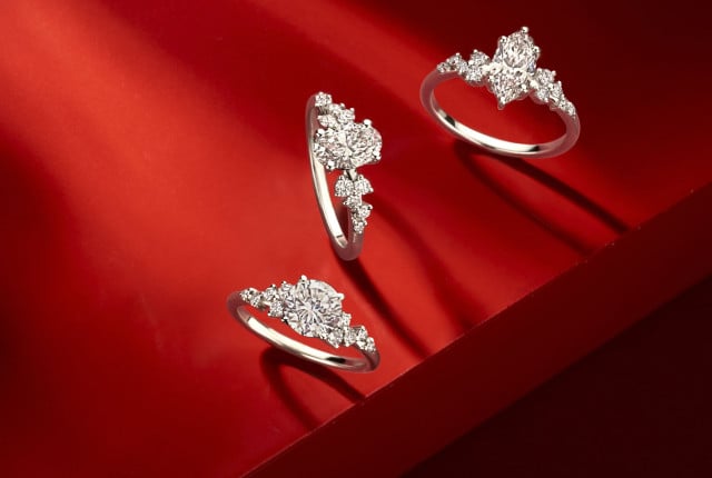 Three white gold engagement rings with round and oval lab grown diamonds on a red display