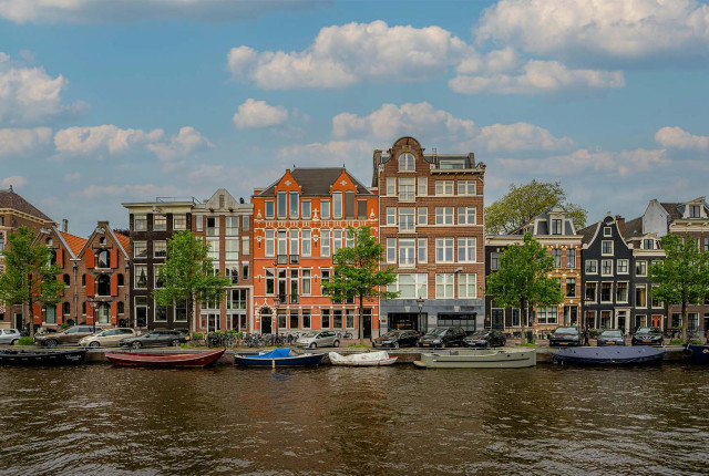 Amsterdam canal view with historic gabled townhouses, moored boats, and a blue sky