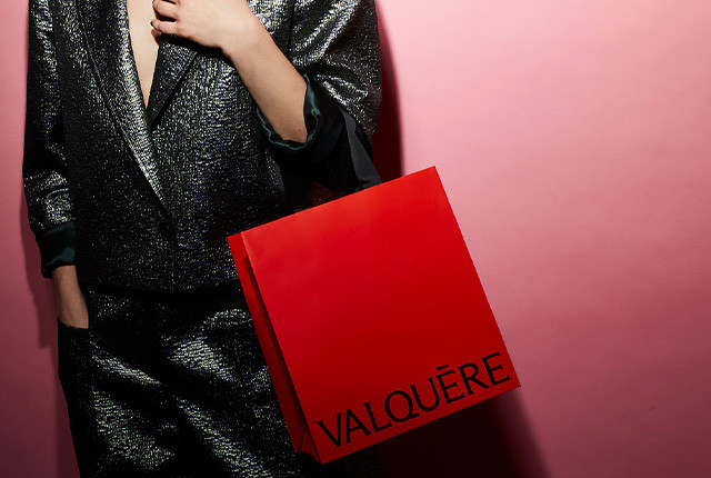 Sac cadeau rouge Valquère porté à la main, image de marque sur fond rose.