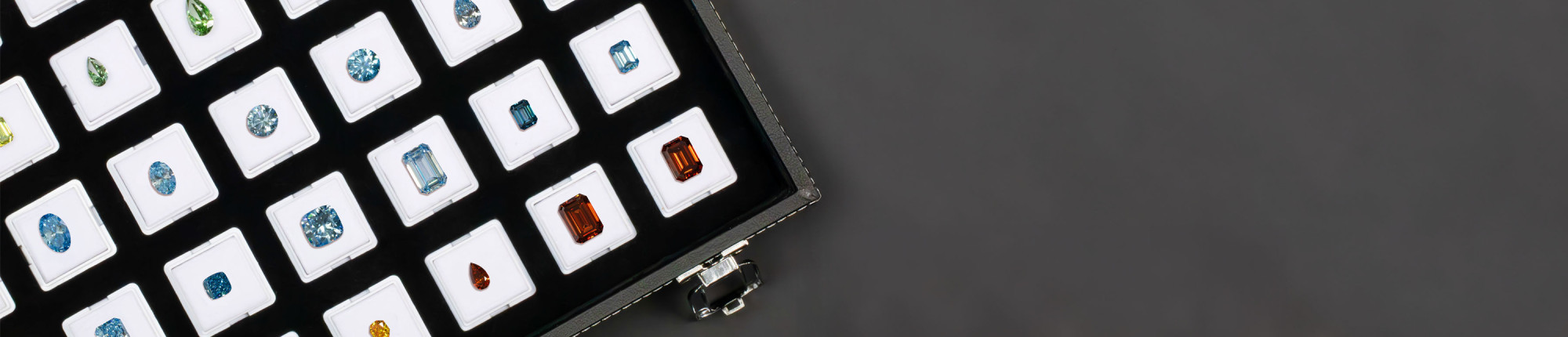 Écrin noir ouvert présentant des diamants de couleur taillés en poire, rond et émeraude sur supports blancs.