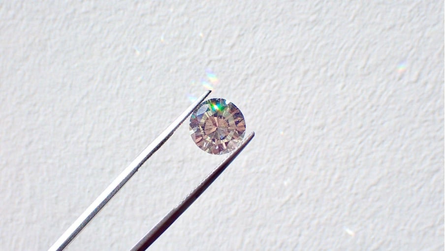 Een fonkelende lab grown diamant met ronde slijpvorm, vastgehouden door een diamanttang.