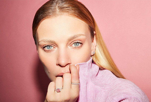 Vrouw met roségouden ring met roze steen en pavé diamanten, plus subtiele diamanten oorknopjes