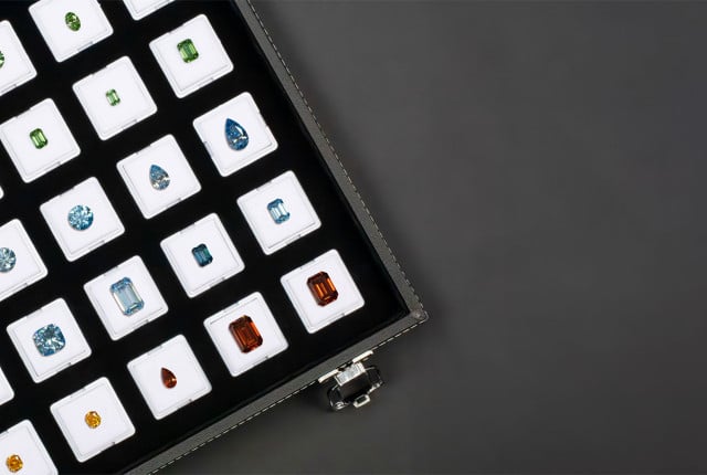 Assortiment van losse gekleurde diamanten in witte doosjes, met groene, blauwe en oranje stenen